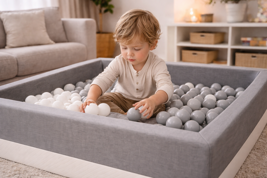 Dreijähriges Kind sortiert weiße und graue Bälle im grauen Bällebad im modernen Wohnzimmer und fördert spielerisch Motorik