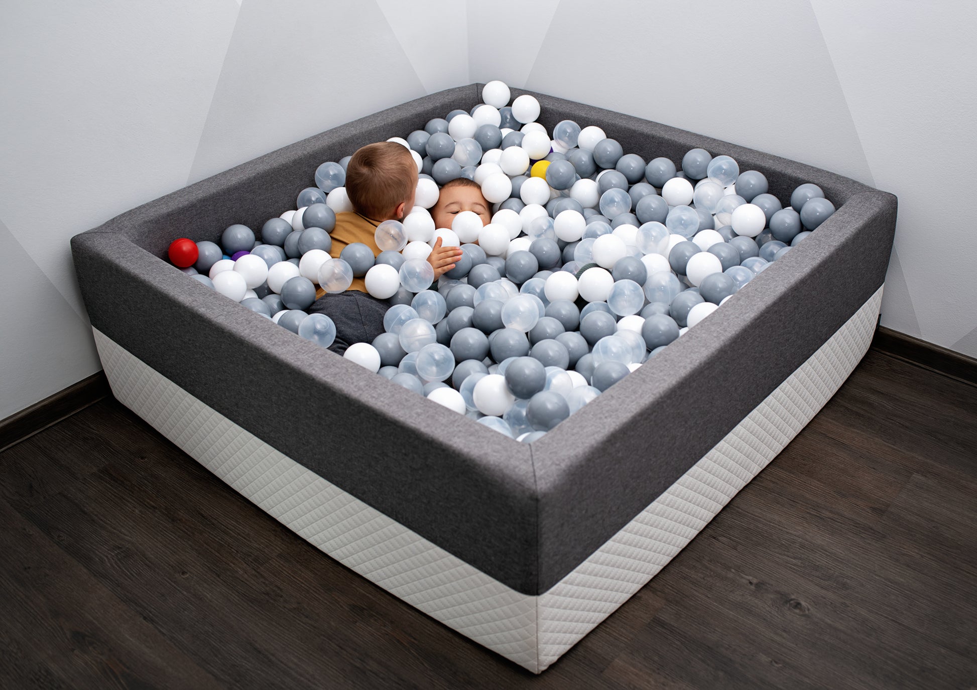 Zwei Kinder spielen im grauen XXL Bällebad mit weißen und grauen Bällen im Kinderzimmer